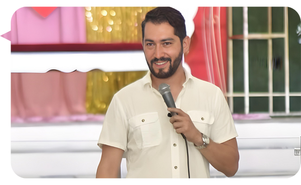 Mario de Paz sonriente, sosteniendo un micrófono mientras imparte una conferencia en un entorno colorido y acogedor.